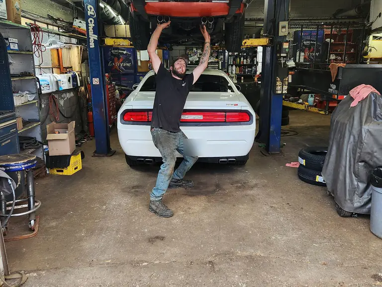 A Mountain Automotive technician standing beneath a car raised on the shop hoist