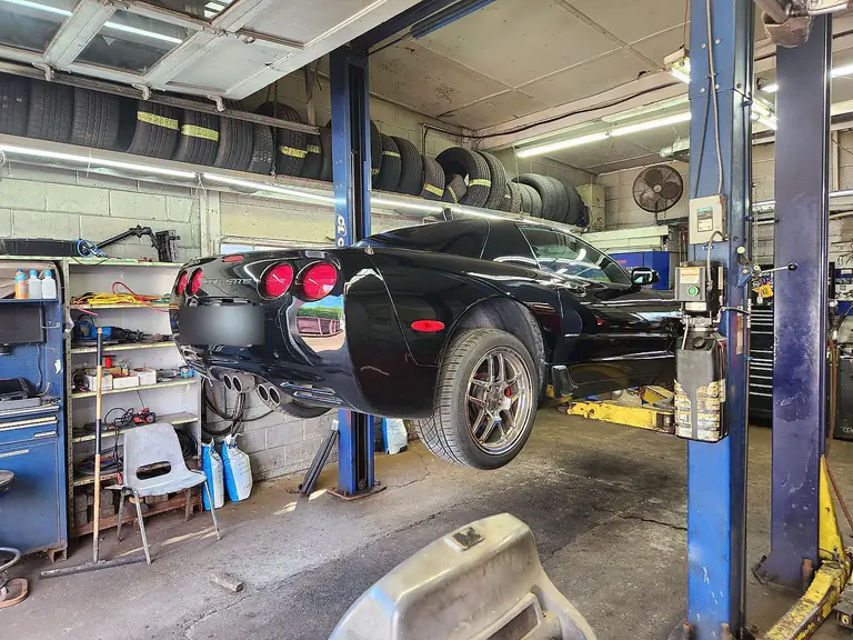 A car raised on the two-post hoist with racks of tyres along the workshop wall
