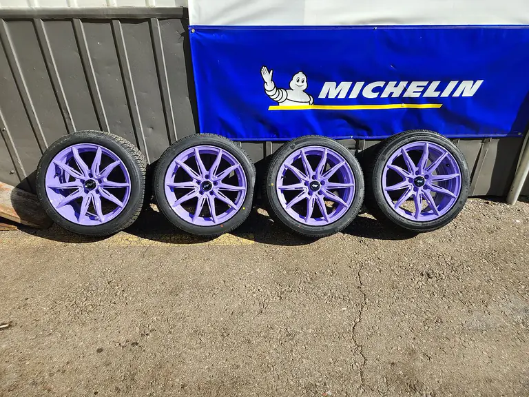 A set of four alloy wheels and tyres lined up against a Michelin banner outside the shop
