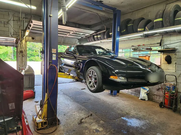A sports car raised on the two-post hoist, with racks of tyres along the wall behind it
