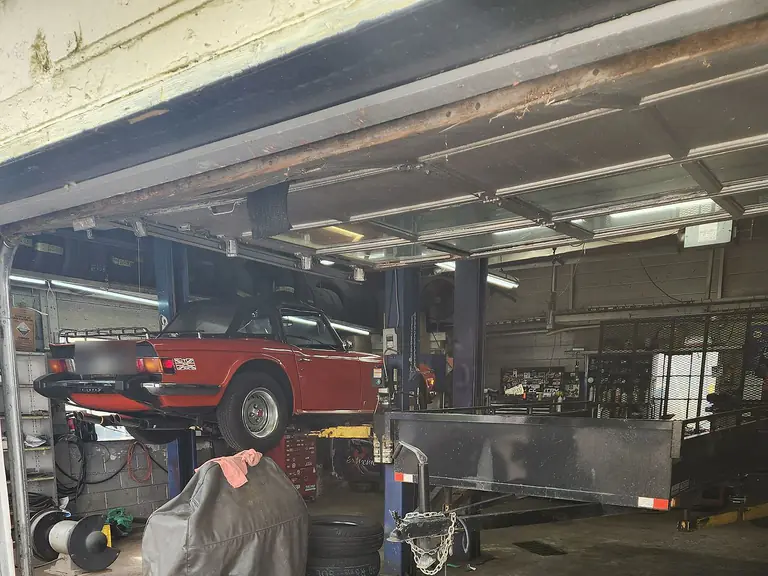A classic car raised on the hoist, seen through the open bay door